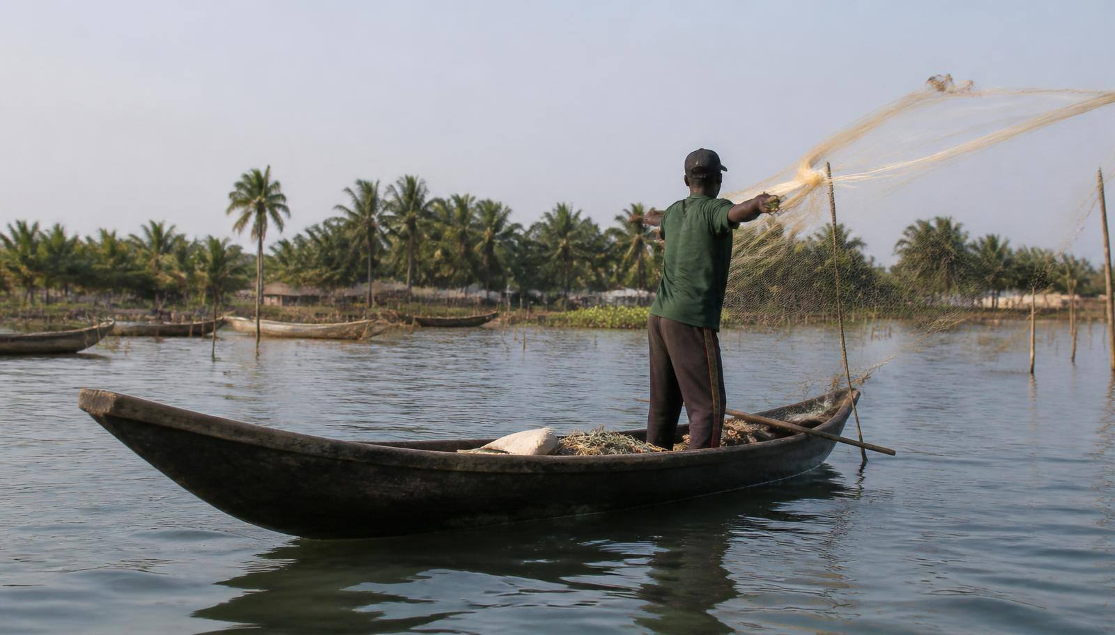 Pêcheur lançant son filet depuis une pirogue traditionnelle sur la lagune